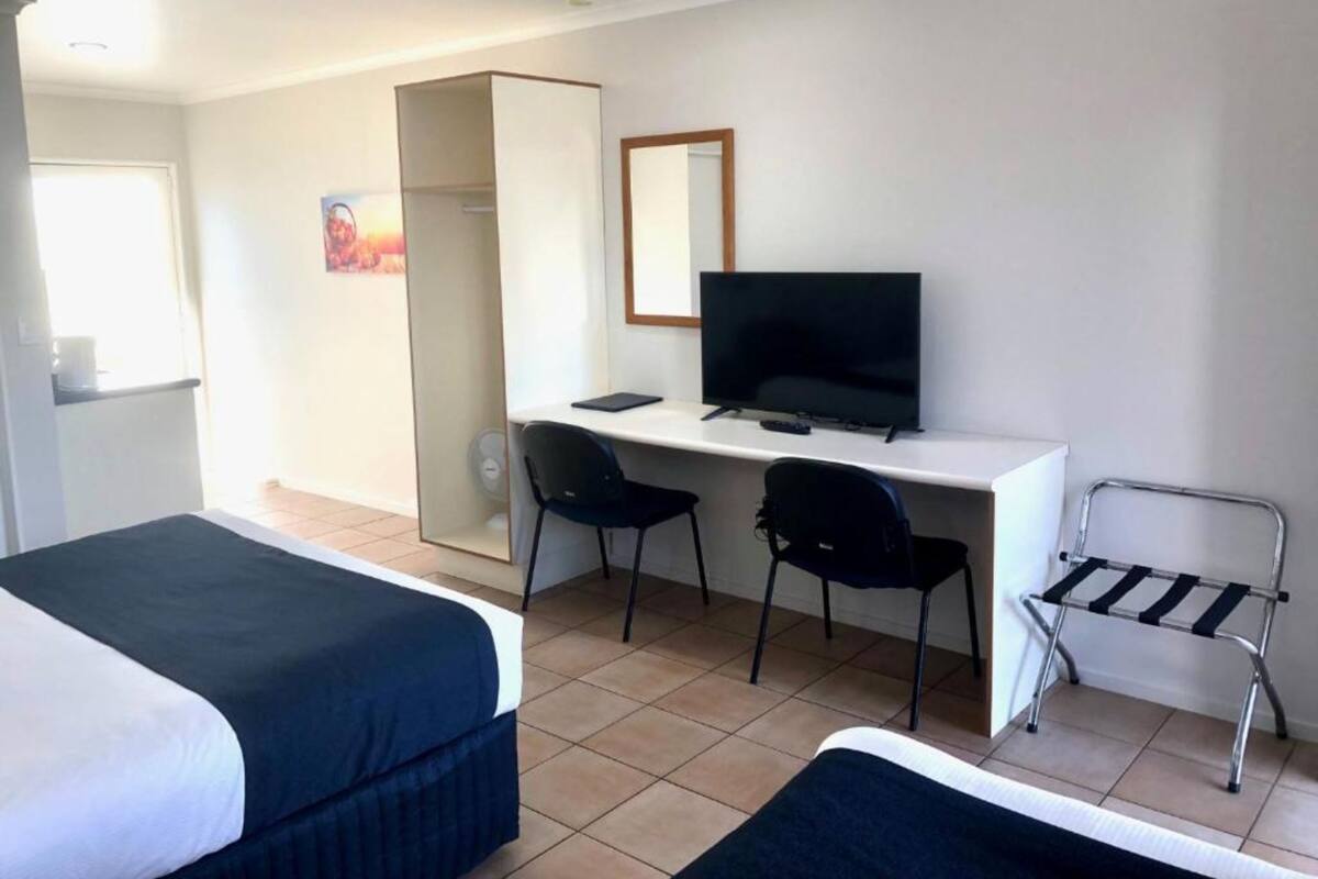 A hotel room with two beds, a desk with a TV, and a chair.