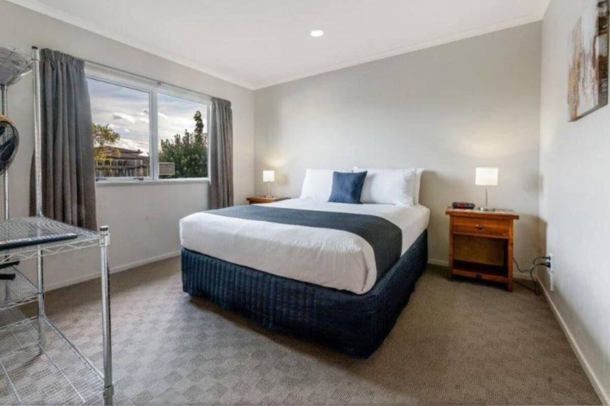 A hotel room with a large bed, two bedside tables, a window with curtains, and a view of the outside.