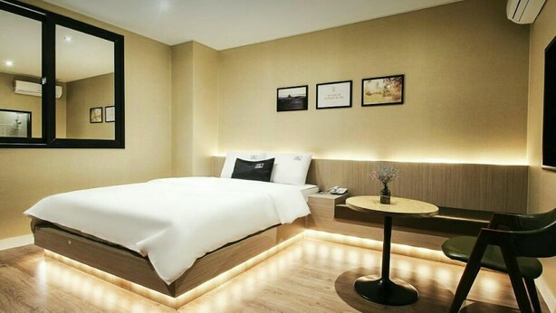 A modern hotel room with a large bed, bedside table, and a small round table with a chair. - The Hotel Changwon (Changwon)