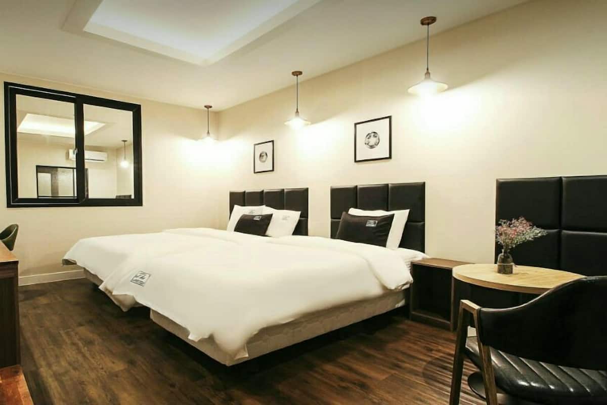 Una habitación de hotel con cama, escritorio, silla y una pequeña mesa con un florero.