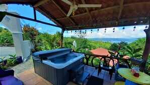 Un patio con jacuzzi, mobiliario exterior y vistas a un paisaje exuberante.