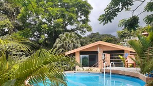 Un área de piscina con un pequeño edificio, rodeada de exuberante vegetación y árboles.