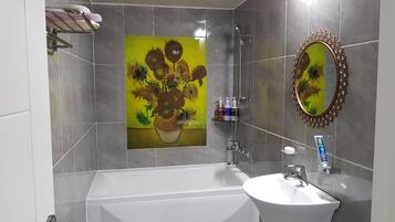 Un baño moderno con bañera, lavabo, espejo y estante empotrado con artículos de aseo.