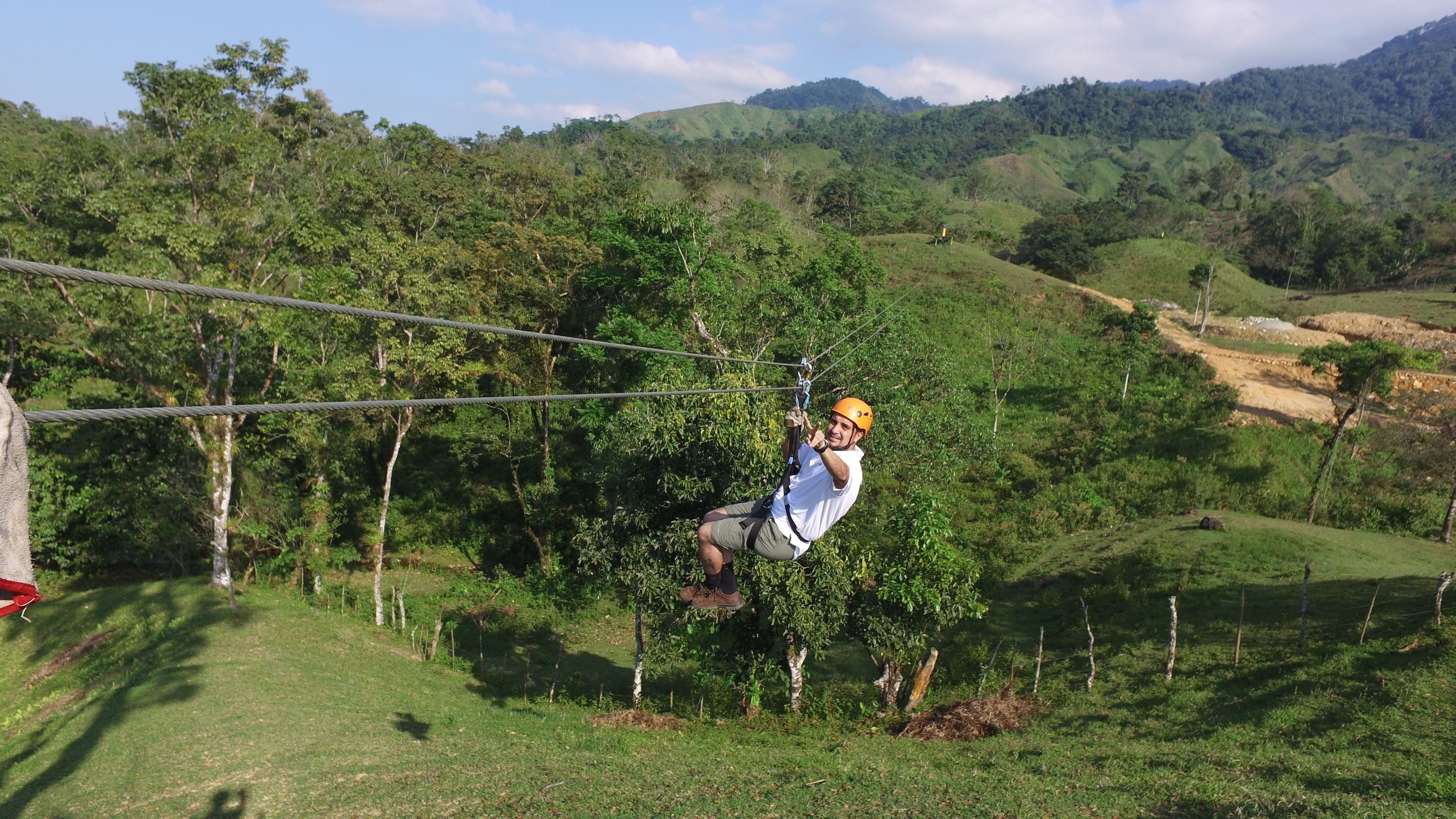 A person zip-lining through a lush, green landscape with hills in the background.