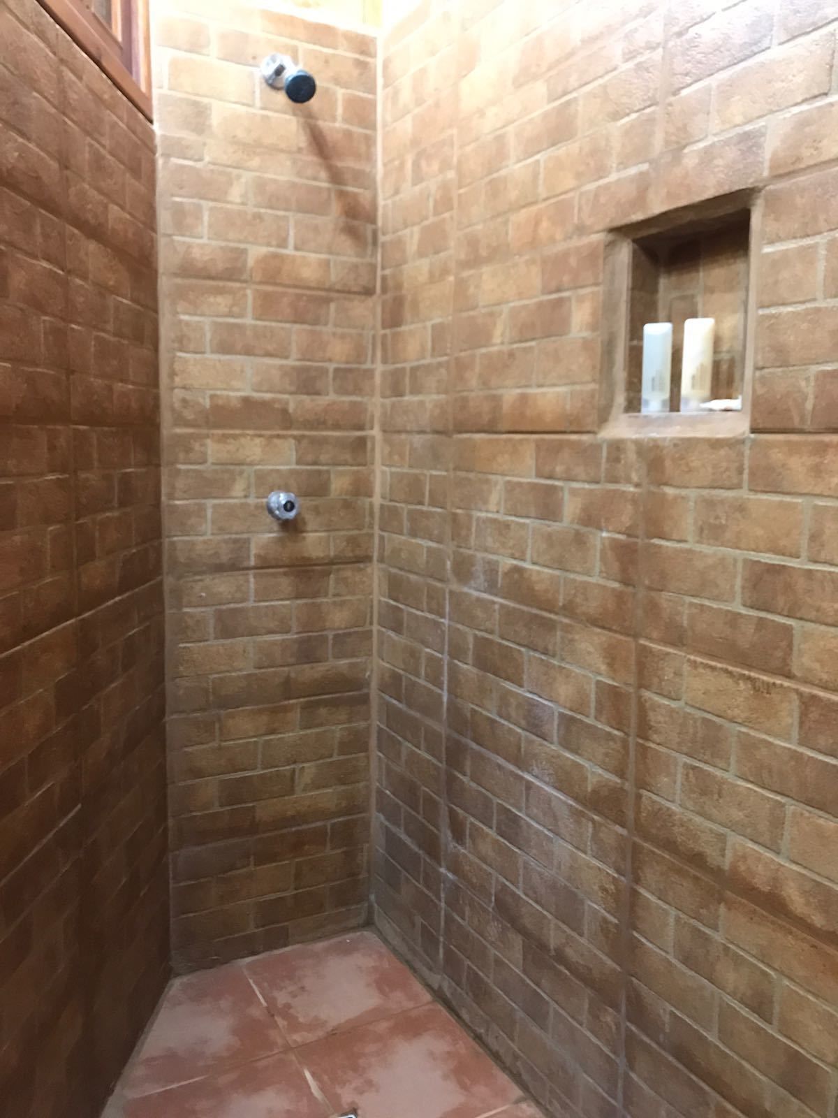 A small, enclosed shower area with brick walls and a tiled floor.