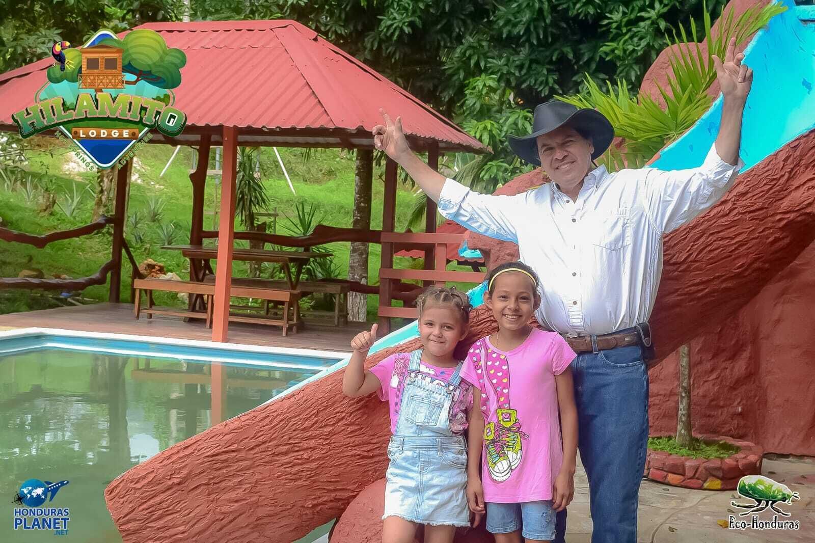 A man and two children at a lodge with a pool and a wooden deck.