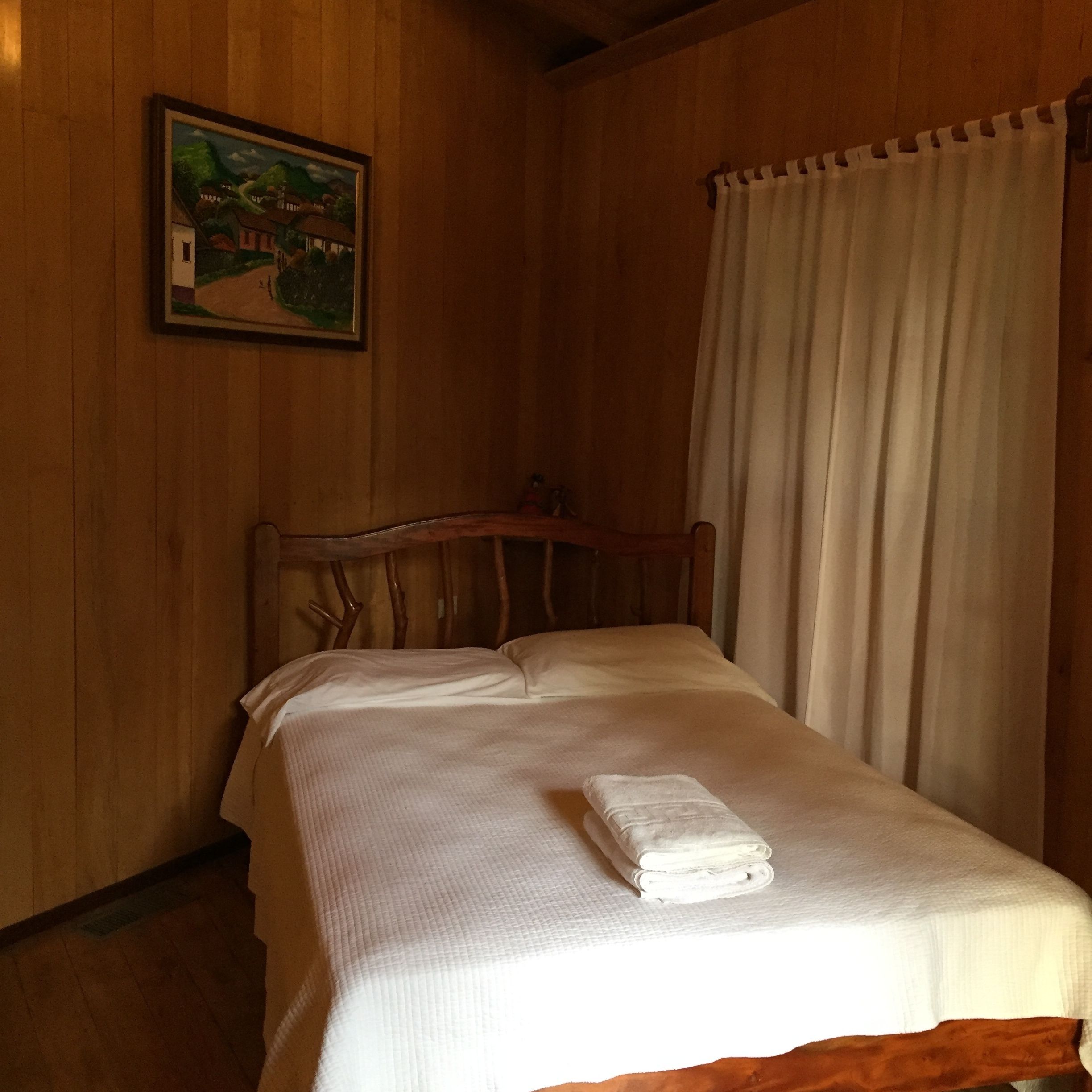 A wooden room with a bed, a painting on the wall, and a curtain.