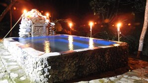 A stone hot tub surrounded by a stone wall, with candles and a small waterfall feature.