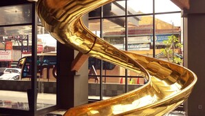 A spiral golden sculpture in a lobby with a checkered floor and large windows. - ARTOTEL Yogyakarta (Depok)