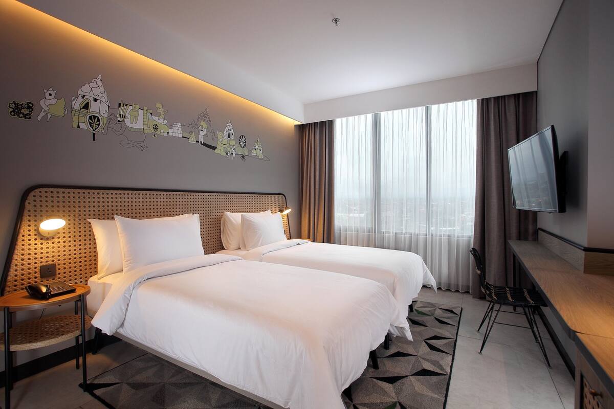 A hotel room with two beds, a TV, a desk, and a wall with decorative stickers.