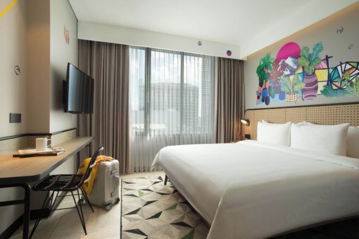 Una habitación de hotel con una cama grande, un escritorio con silla, un televisor y una ventana con cortinas.