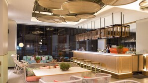 A modern bar area with wicker furniture, a bar counter, and pendant lighting. - ARTOTEL Yogyakarta (Depok)