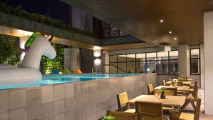 An indoor pool area with a large inflatable unicorn sculpture, surrounded by dining tables and chairs. - ARTOTEL Yogyakarta (Depok)