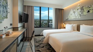A hotel room with two beds, a desk with a chair, a TV, and a large window offering a city view. - ARTOTEL Yogyakarta (Depok)