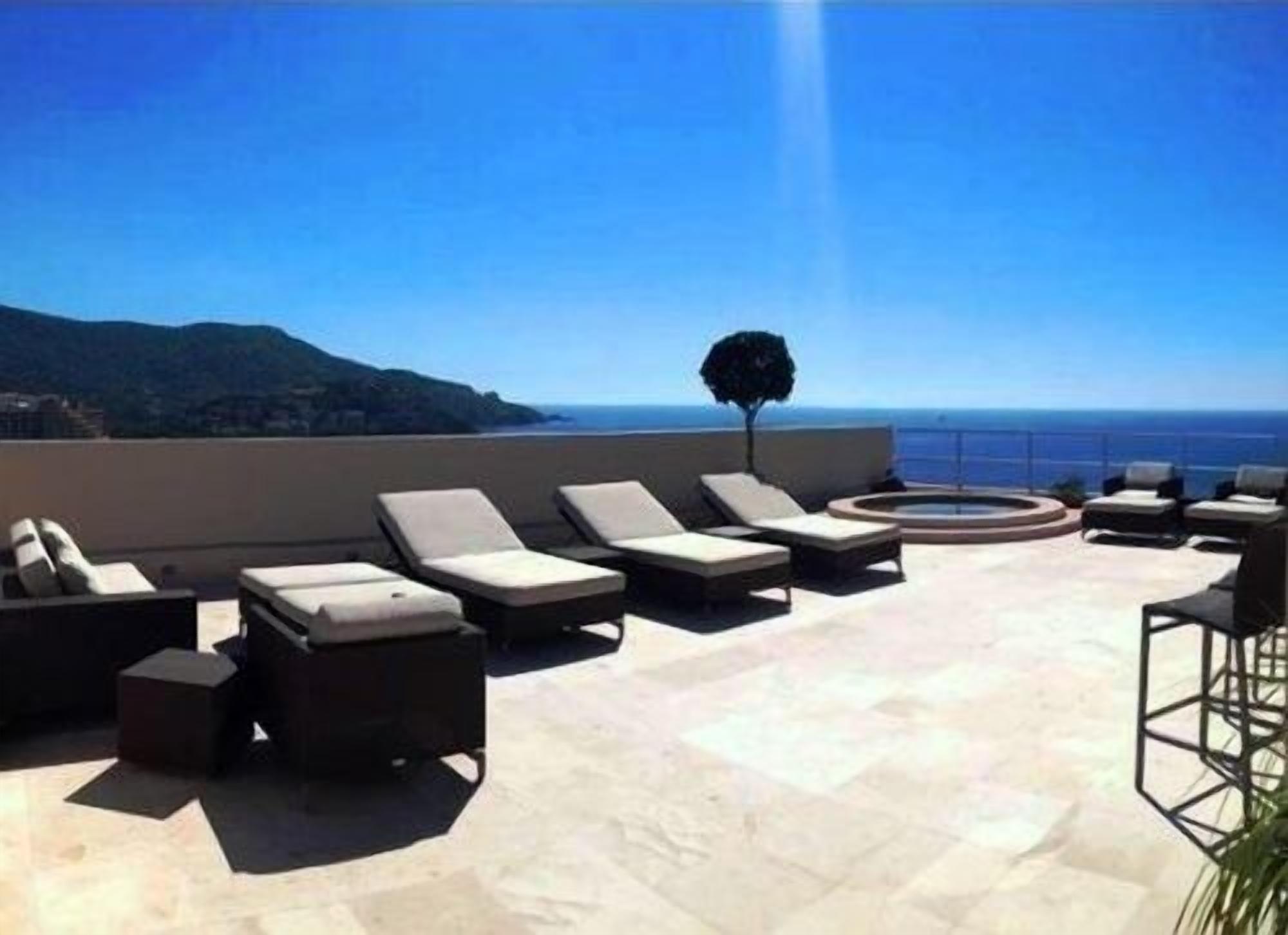 A rooftop terrace with lounge chairs and a circular seating area, overlooking a coastal landscape.