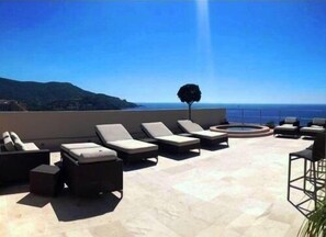 A rooftop terrace with lounge chairs and a circular seating area, overlooking a coastal landscape.