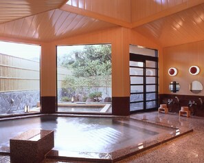 Un onsen japonés tradicional con una fuente termal de piedra, interior de madera y vista a un jardín.