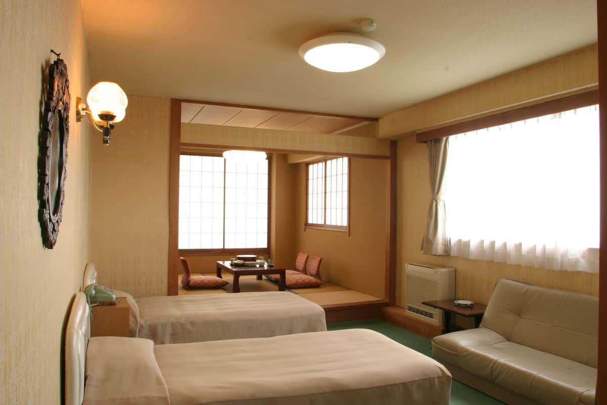 A hotel room with two beds, a sofa, a small table, and a window with curtains.