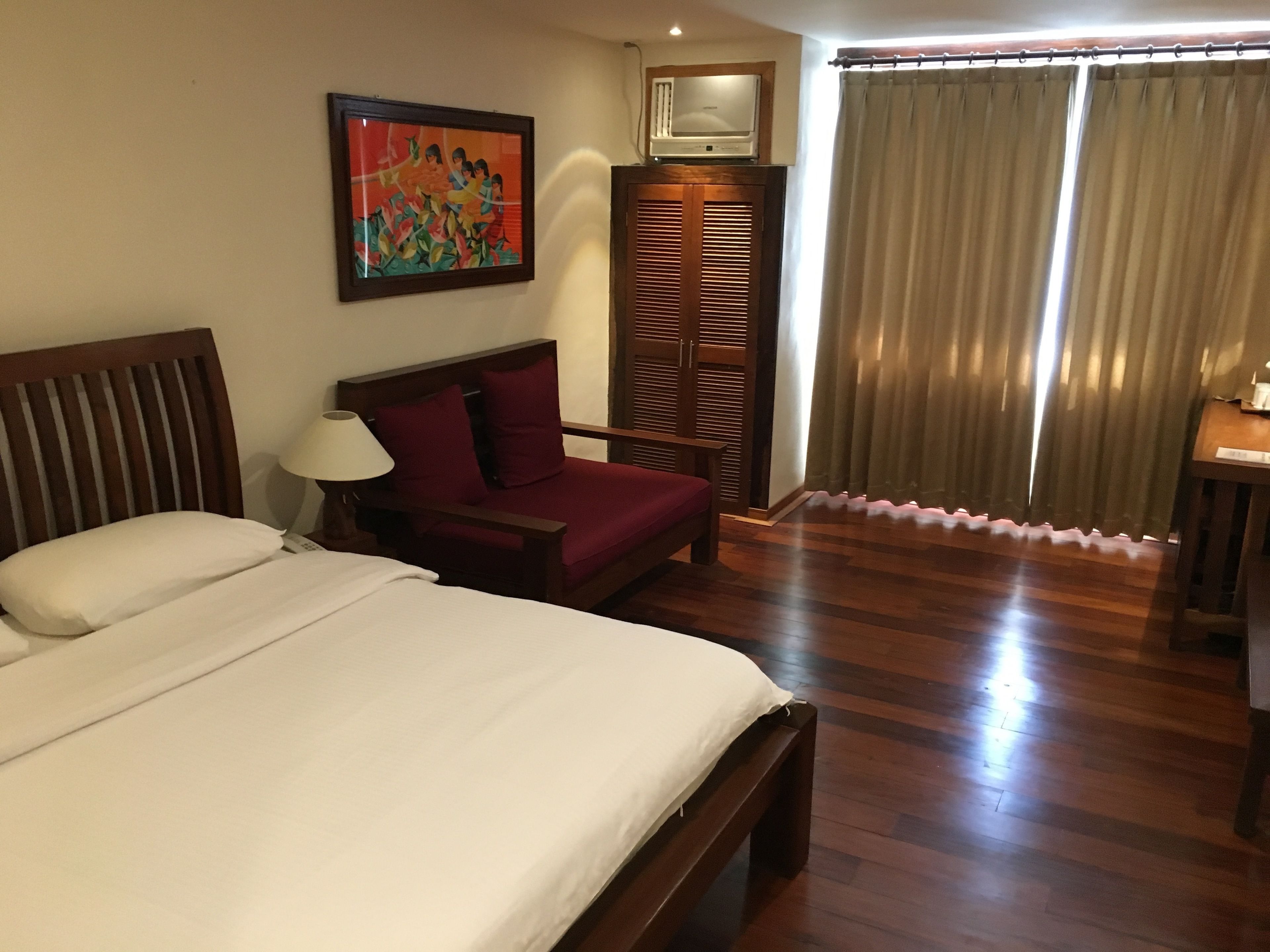 A hotel room with a bed, a chair, a desk, a TV, and a window with curtains.