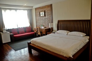 Une chambre d’hôtel avec un grand lit, un canapé rouge, un bureau avec une lampe et un mur en briques.