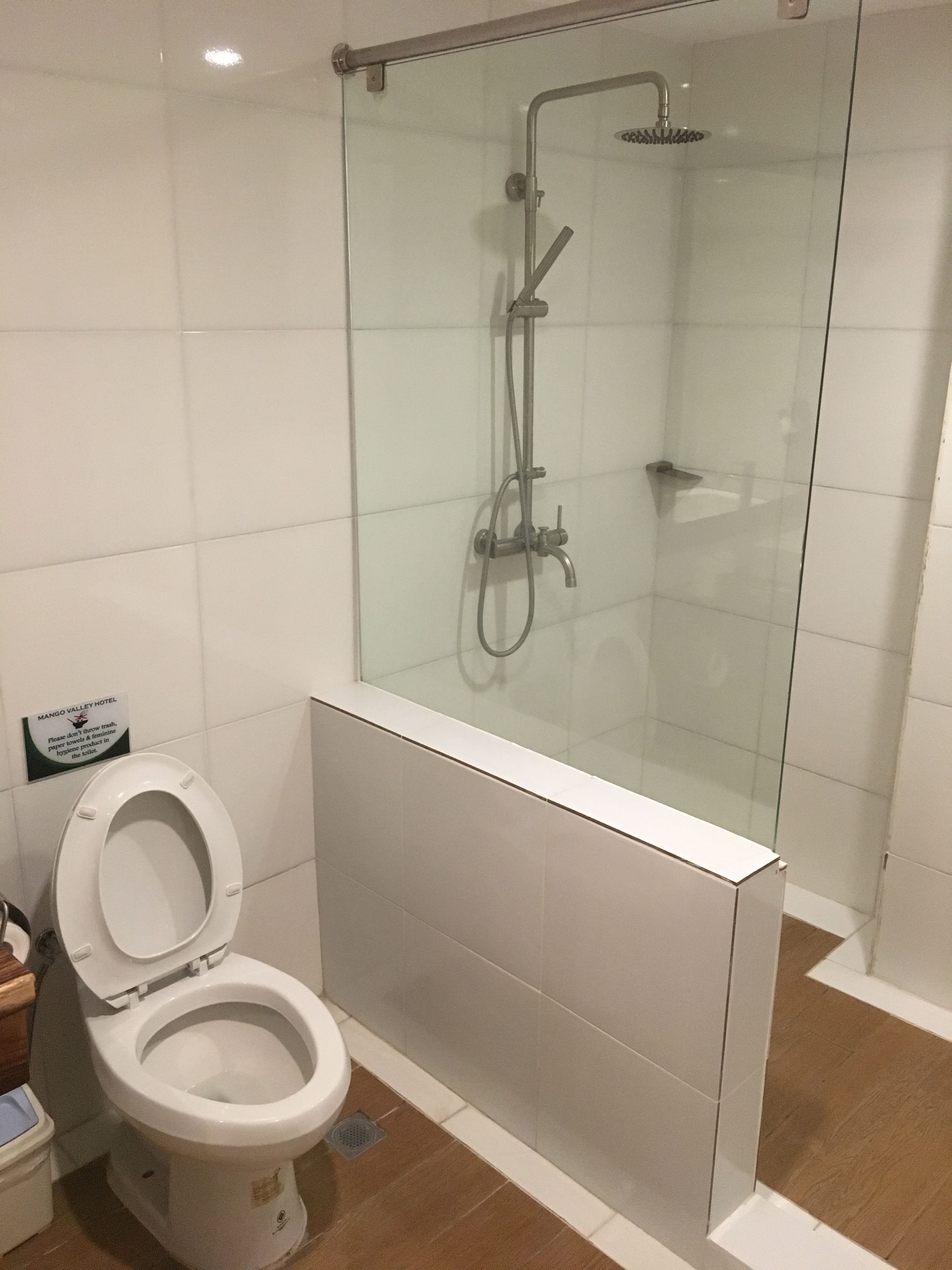 A modern bathroom with a glass-enclosed shower, a toilet, and a sign indicating the hotel name.
