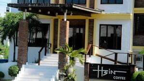Un edificio de dos pisos con fachada amarilla y blanca, entrada de ladrillo y un letrero que dice "H3N Coffee".