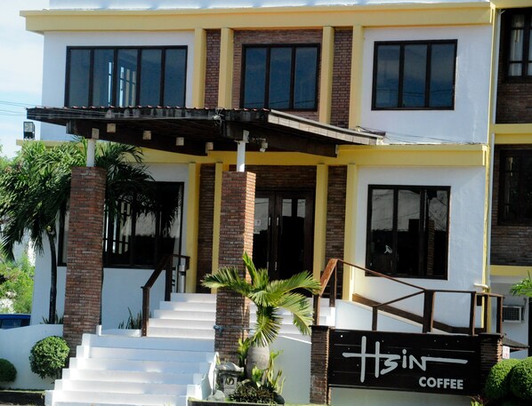 Un bâtiment à deux étages, avec une façade jaune et blanche, une entrée en briques et une enseigne indiquant « H3N Coffee ».