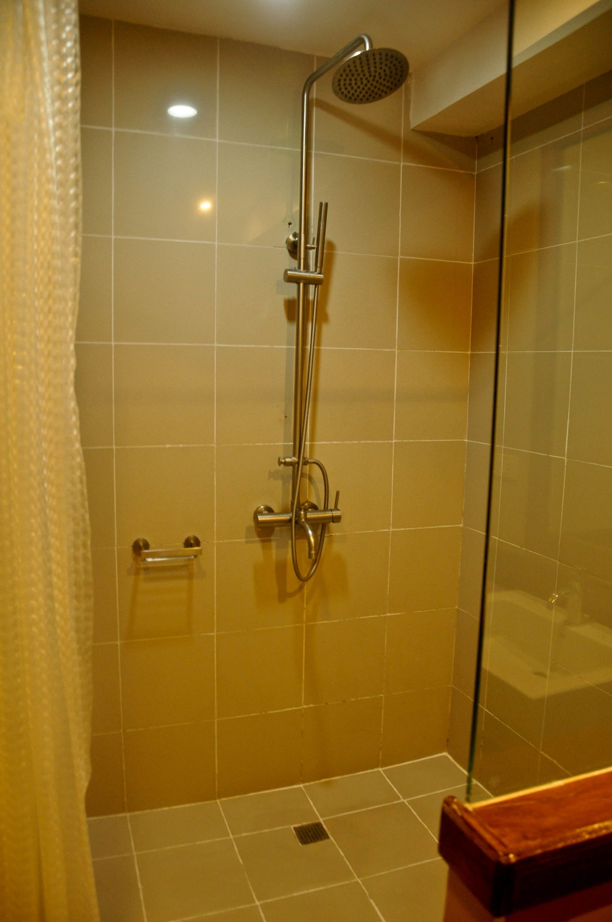 Ducha con puerta de vidrio, cabezal de ducha de mano y panel de control en la pared.