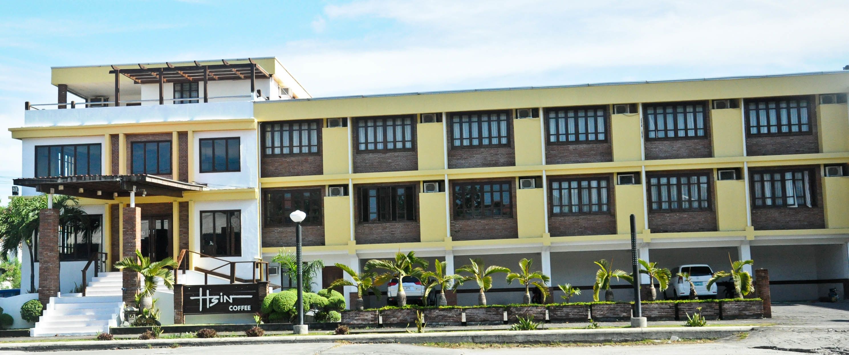 A multi-story building with a coffee shop on the ground floor, multiple balconies, and a parking area with cars.