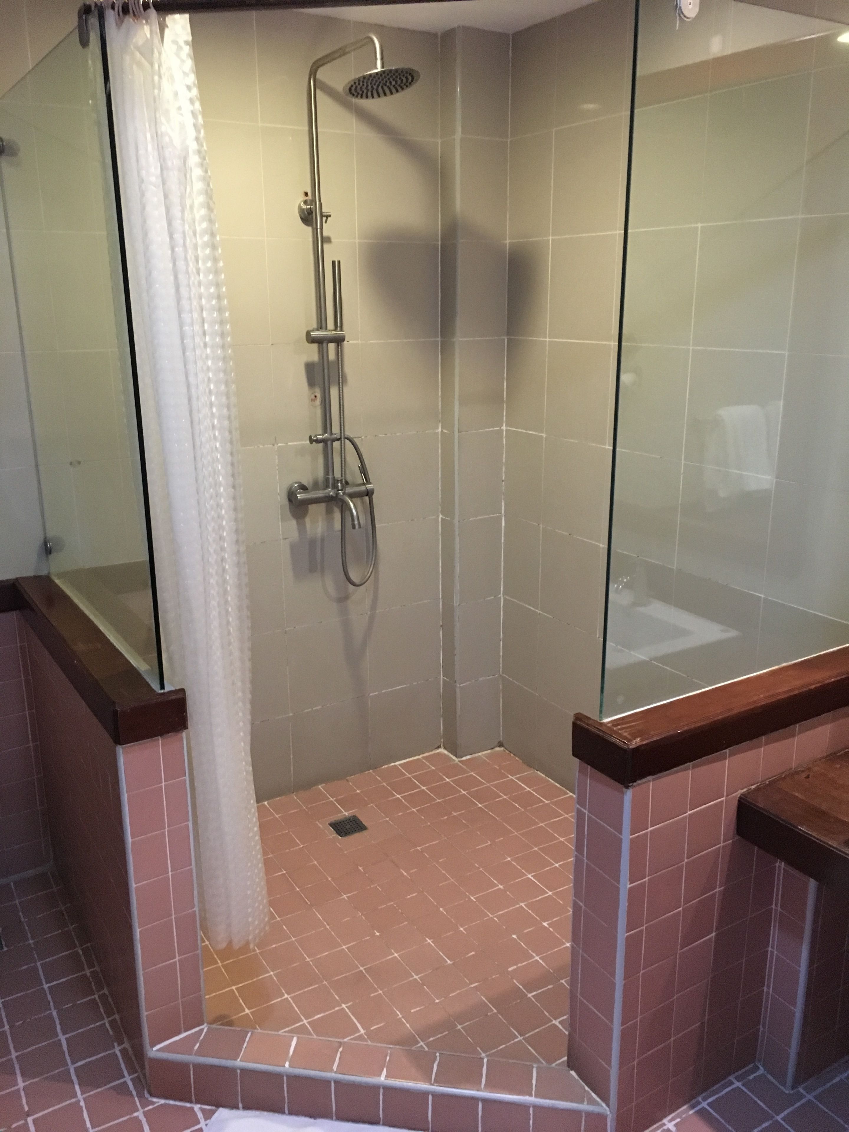 A glass-enclosed shower with a handheld showerhead, tiled walls, and a brown-tiled floor.