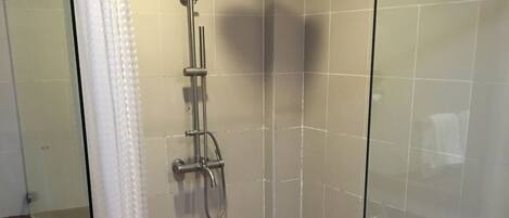 A glass-enclosed shower with a handheld showerhead, tiled walls, and a brown-tiled floor.