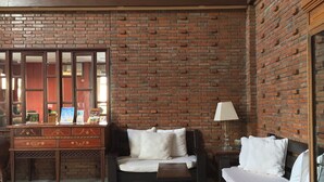 Una habitación con pared de ladrillo, un escritorio de madera con cajones, un sofá, una mesita y una lámpara.