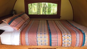 A bed with a patterned bedspread and pillows in a tent-like room with a window. - Greytown Campground (Greytown)