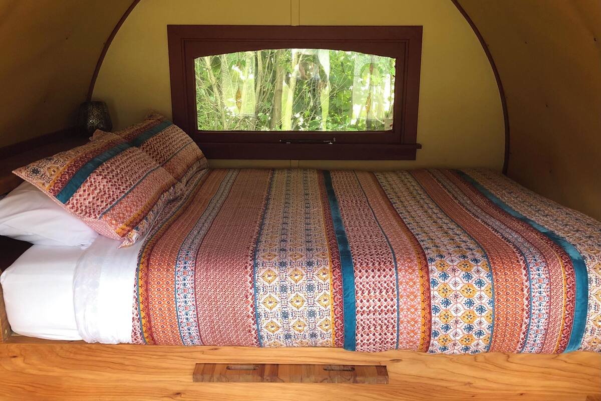 A bed with a patterned bedspread and pillows in a tent-like room with a window.