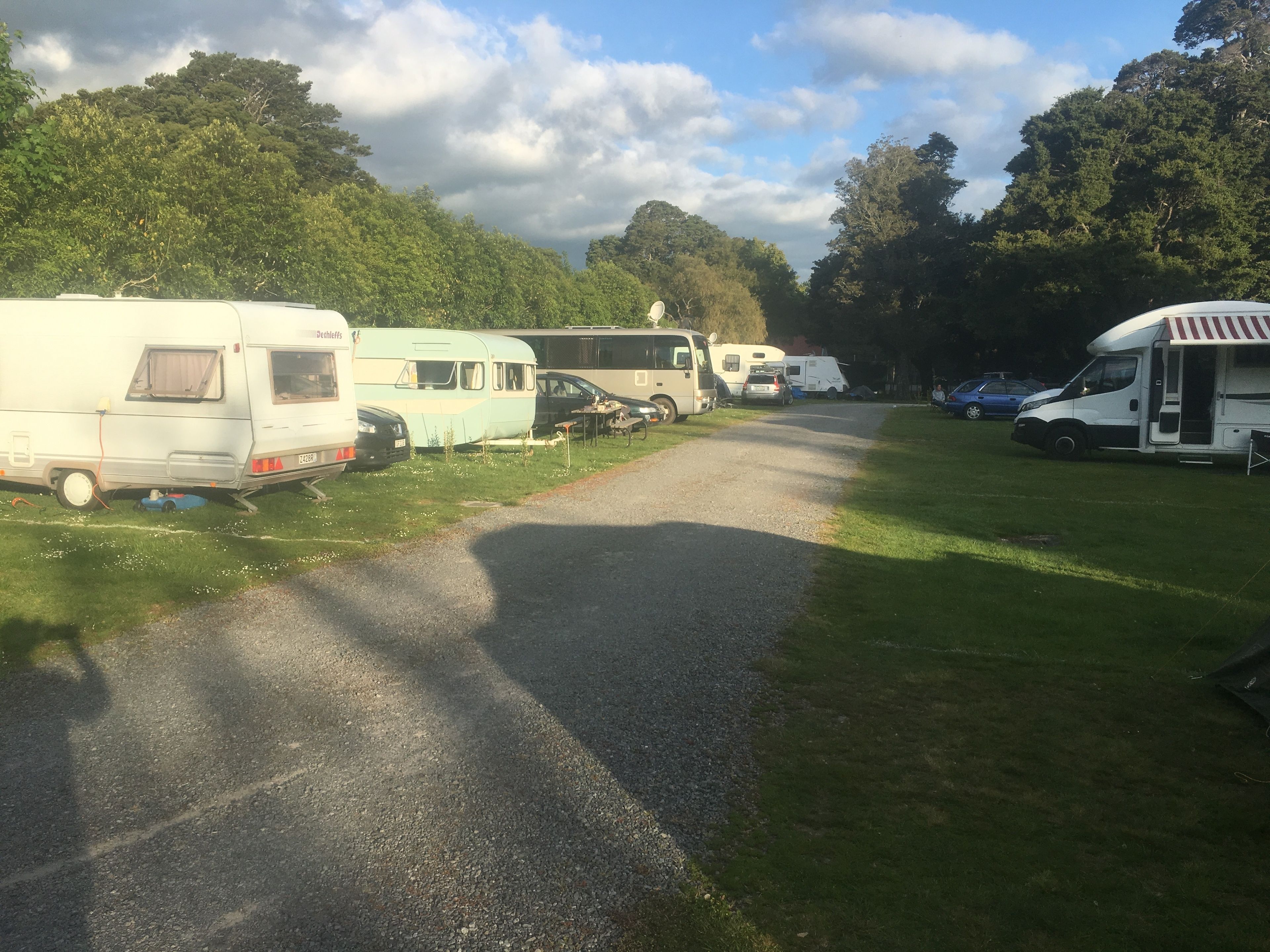 A campsite with RVs parked on a gravel path surrounded by grass and trees.