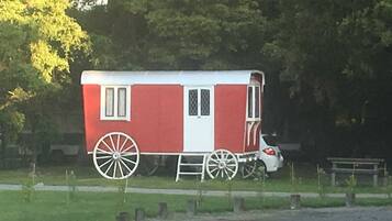 A red and white carriage with large wheels, parked on a grassy area with trees in the background.