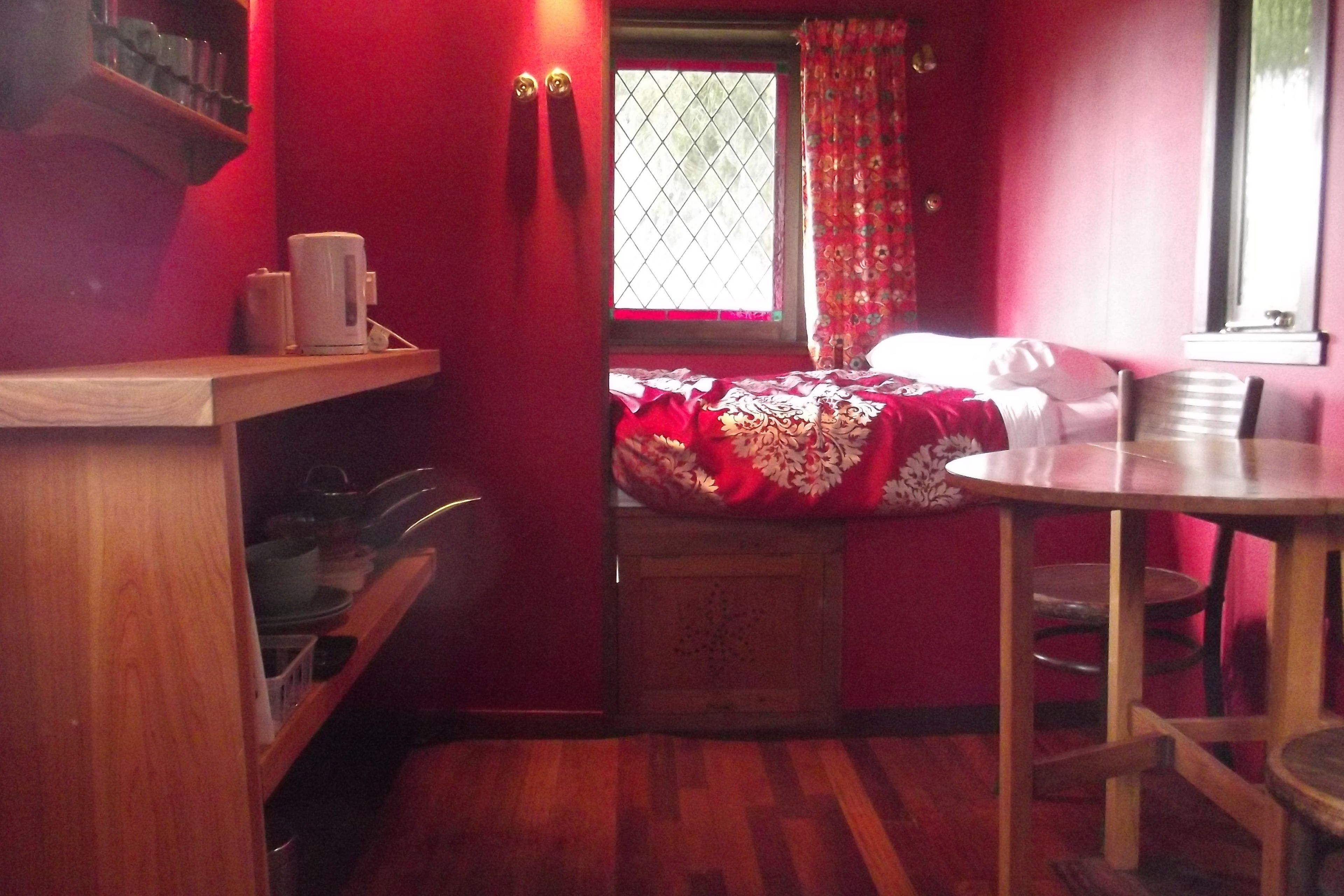 A small, cozy room with a bed, a wooden table, and a window with curtains.
