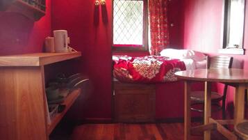 Una habitación pequeña y acogedora con una cama, una mesa de madera y un ventanal con cortinas.