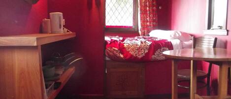 A small, cozy room with a bed, a wooden table, and a window with curtains.