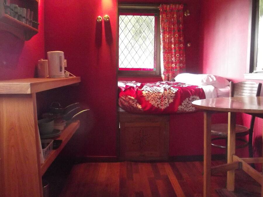 Una habitación pequeña y acogedora con una cama, una mesa de madera y un ventanal con cortinas.