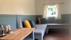 A cozy room with a wooden table, two stools, a bench with cushions, and a window with curtains. - Greytown Campground (Greytown)