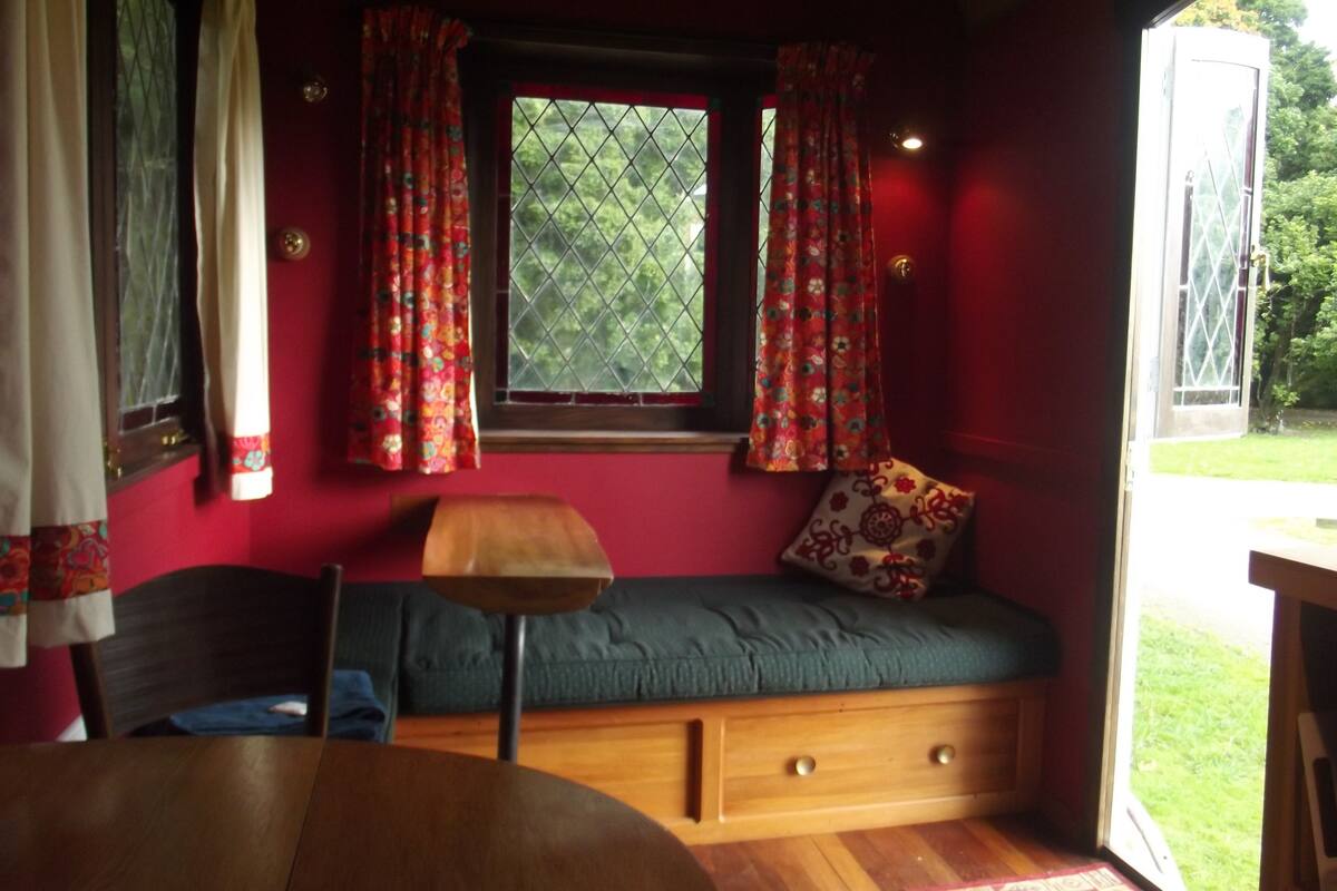 A cozy room with a wooden bench, a small table, and a window with red curtains.
