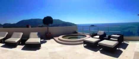 Eine Dachterrasse mit Liegestühlen und einem Whirlpool, mit Blick auf eine gebirgige Landschaft.