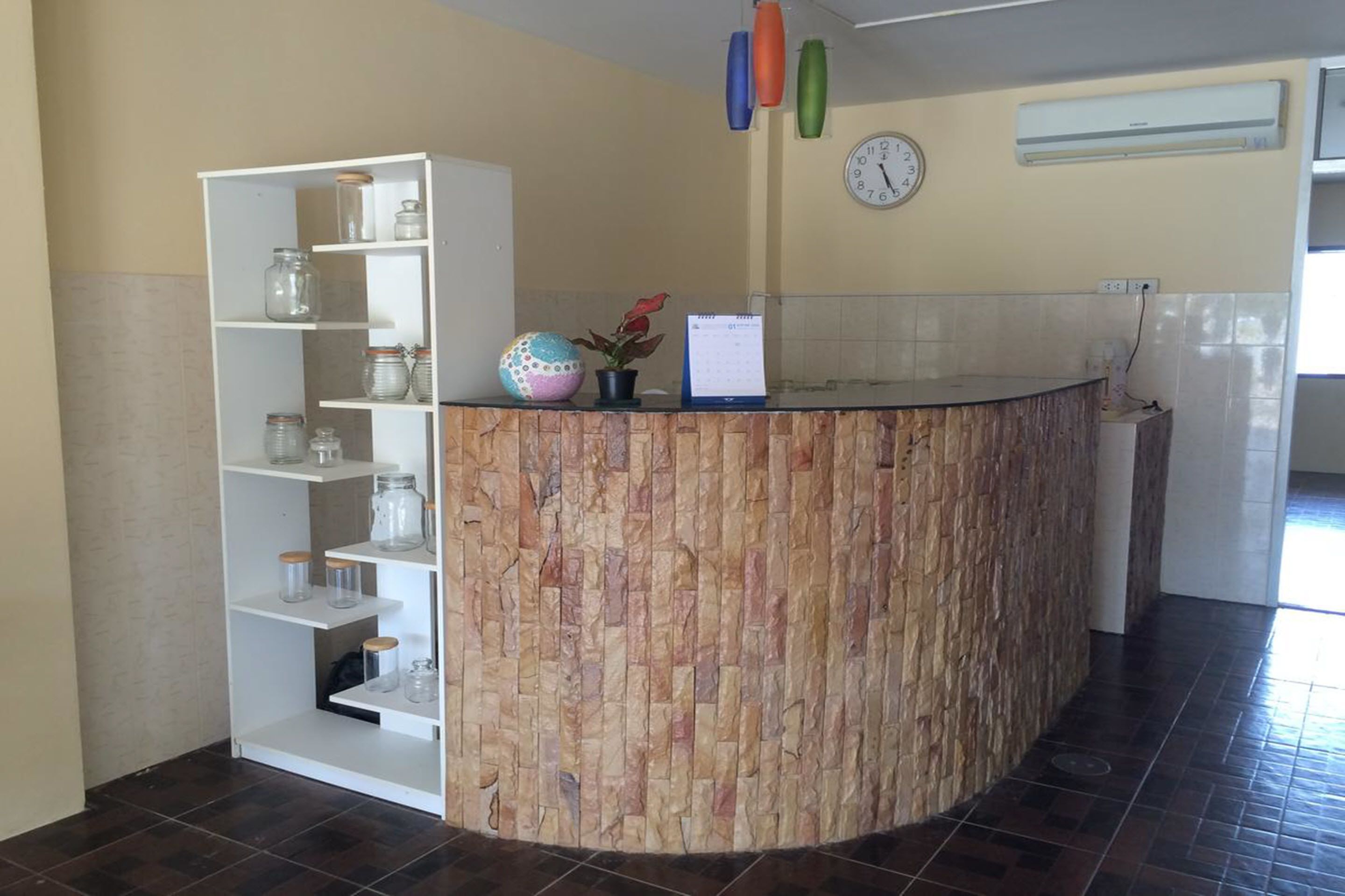 A reception area with a curved counter, a white shelving unit with glass jars, a clock, and an air conditioning unit on the wall.