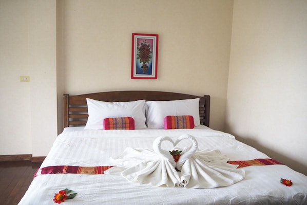 Una cama bien hecha con sábanas blancas, dos almohadas y una toalla dispuesta en forma de corazón.