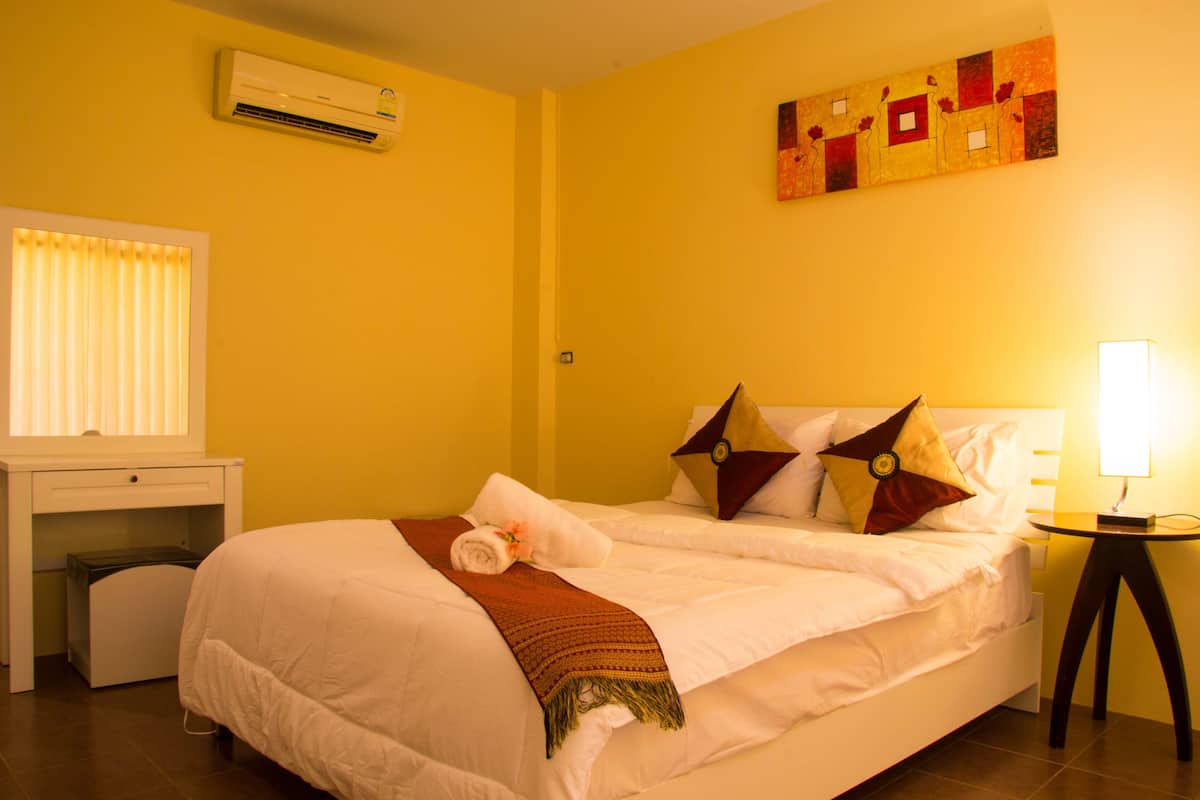 Quarto de hotel com cama, escrivaninha, ar-condicionado, luminária e um quadro na parede.