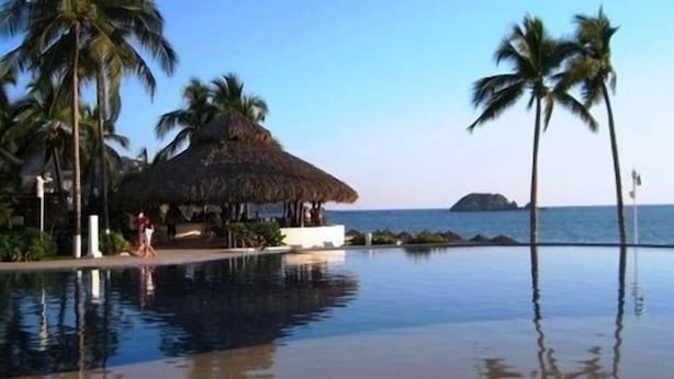 Una piscina con una estructura de techo de paja, palmeras y vista al océano.