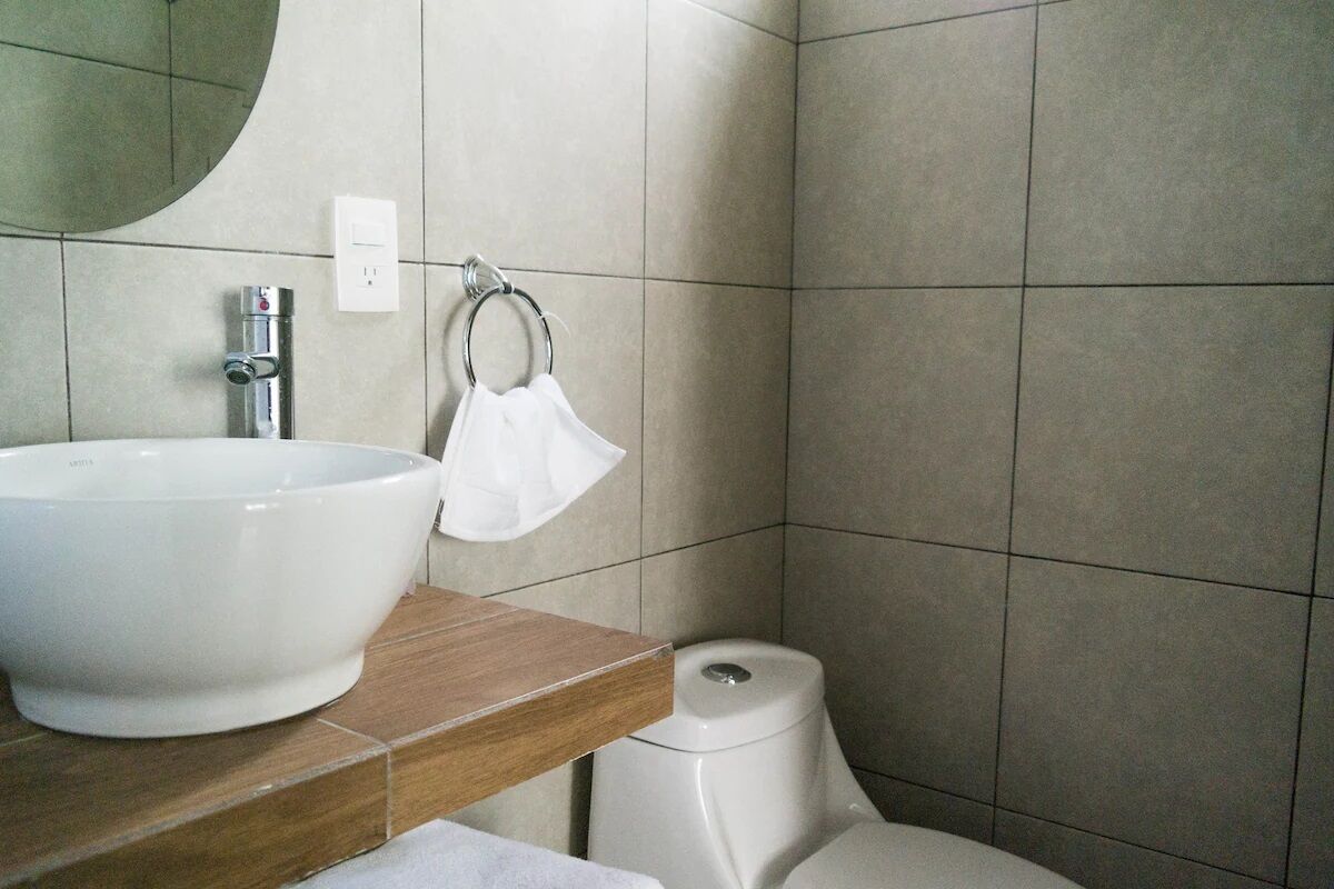 Ein Badezimmer mit einem großen, weißen Waschbecken, einem Spiegel und einer Toilette.