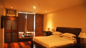 Une chambre d’hôtel avec un lit en bois, une table de chevet avec une lampe, une armoire en bois et une vue sur l’extérieur par une fenêtre avec des rideaux.