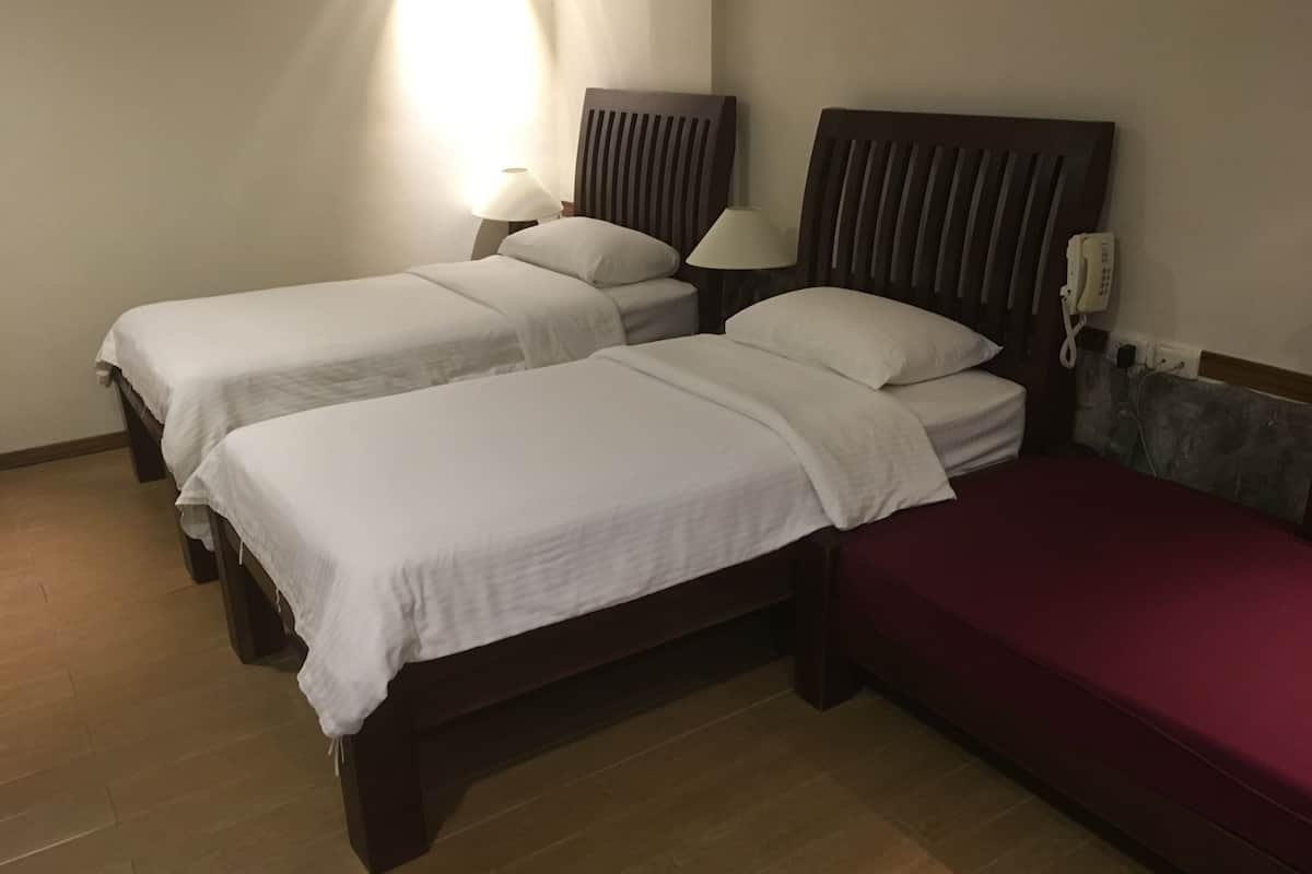 A hotel room with two single beds, a red bed, a wooden headboard, a bedside lamp, and a phone on the wall.